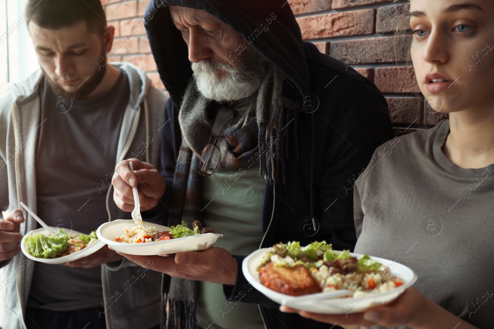 Photo of Poor people with plates of food at wall indoors