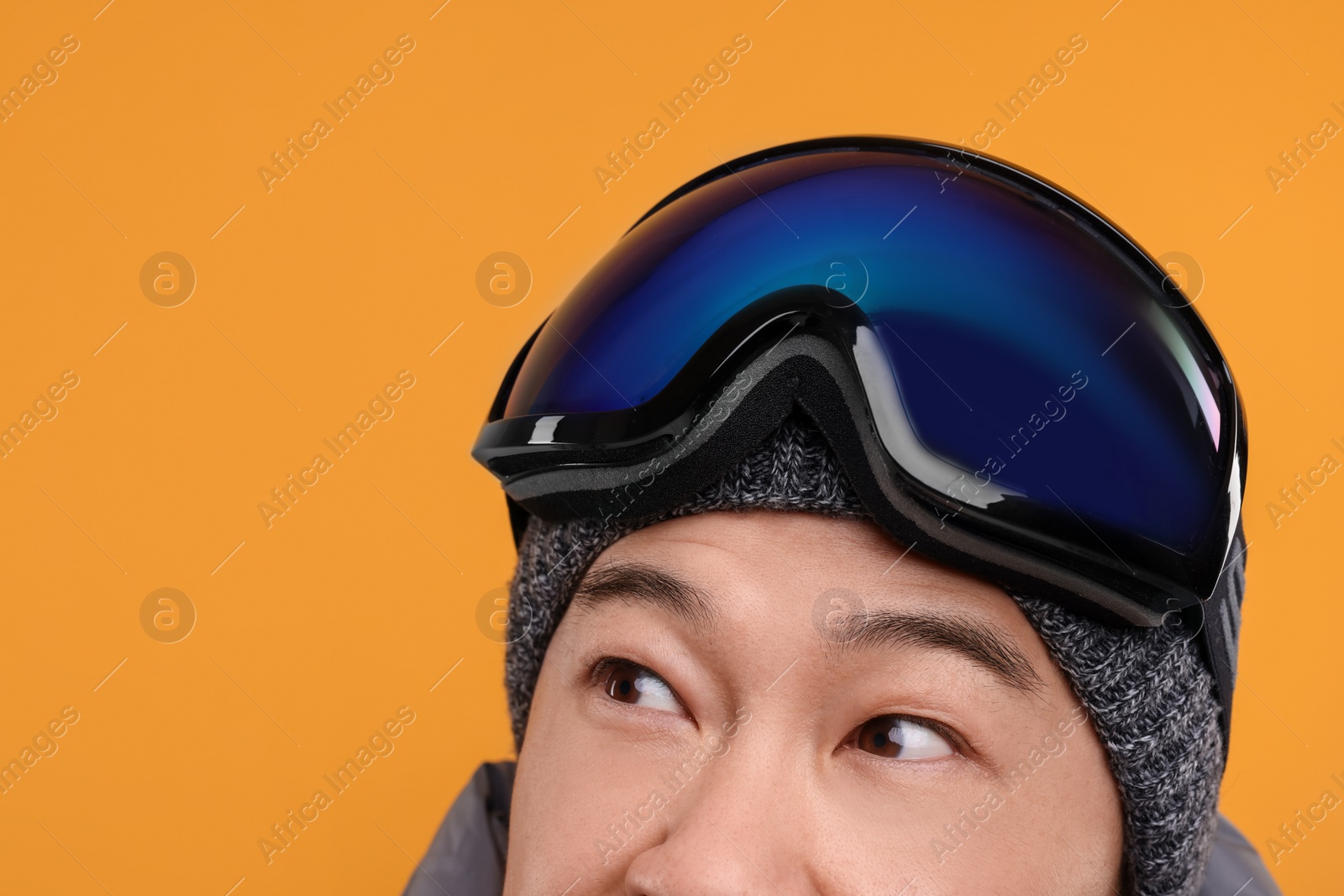 Photo of Winter sports. Man with ski goggles on orange background, closeup. Space for text