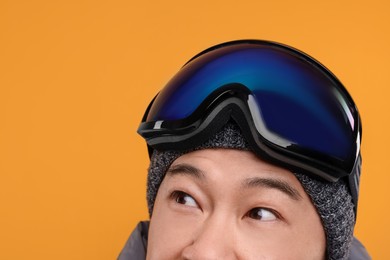 Winter sports. Man with ski goggles on orange background, closeup. Space for text