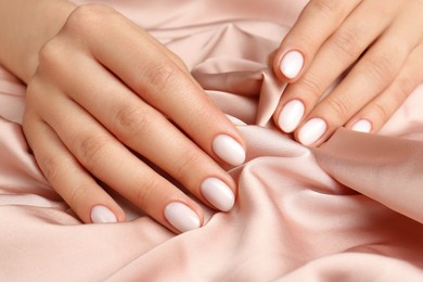 Photo of Woman showing her manicured hands with white nail polish on beige silk fabric, closeup