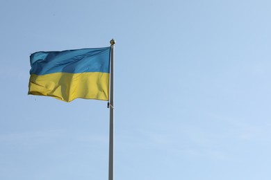 Photo of Flag of Ukraine waving on pole against blue sky. Space for text