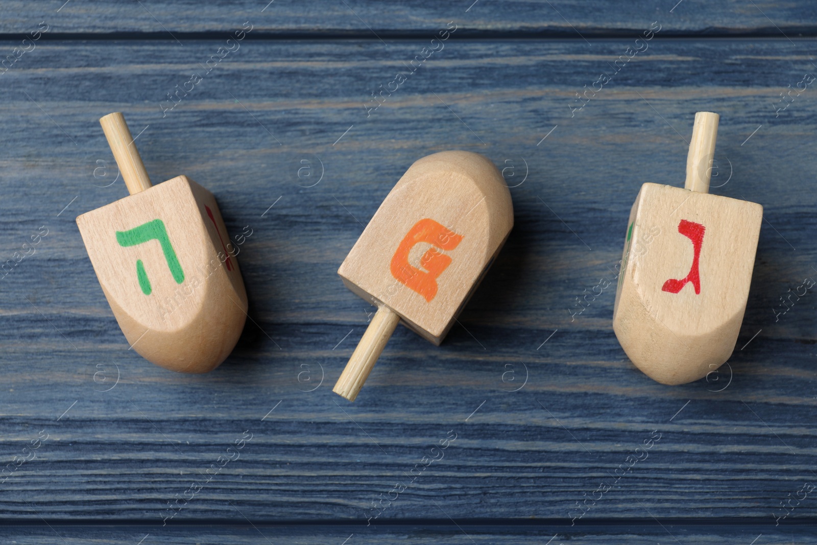 Photo of Hanukkah traditional dreidels with letters He, Pe and Gimel on blue wooden table, flat lay