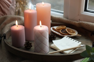 Photo of Tray with burning wax candles and decor on window sill indoors