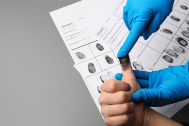 Photo of Investigator taking fingerprints of suspect on grey background, closeup with space for text. Criminal expertise