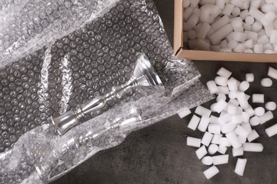 Photo of Elegant silver candlesticks, bubble wrap and cardboard box with foam peanuts on dark grey table, flat lay
