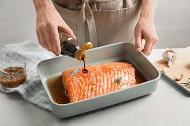 Photo of Woman pouring marinade onto raw salmon in baking dish, closeup