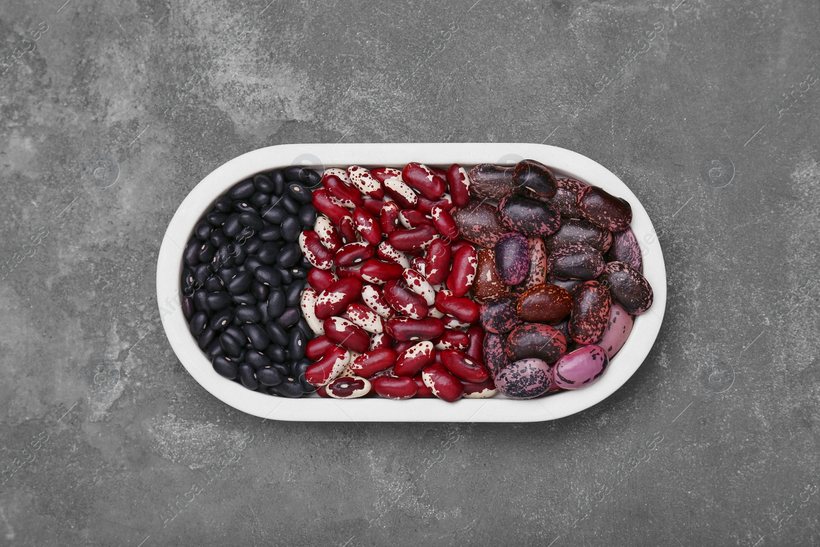 Photo of Plate with different types of beans on grey table, top view