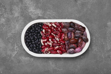 Plate with different types of beans on grey table, top view