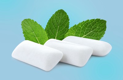 Menthol chewing gum pillows and mint leaves on light blue background