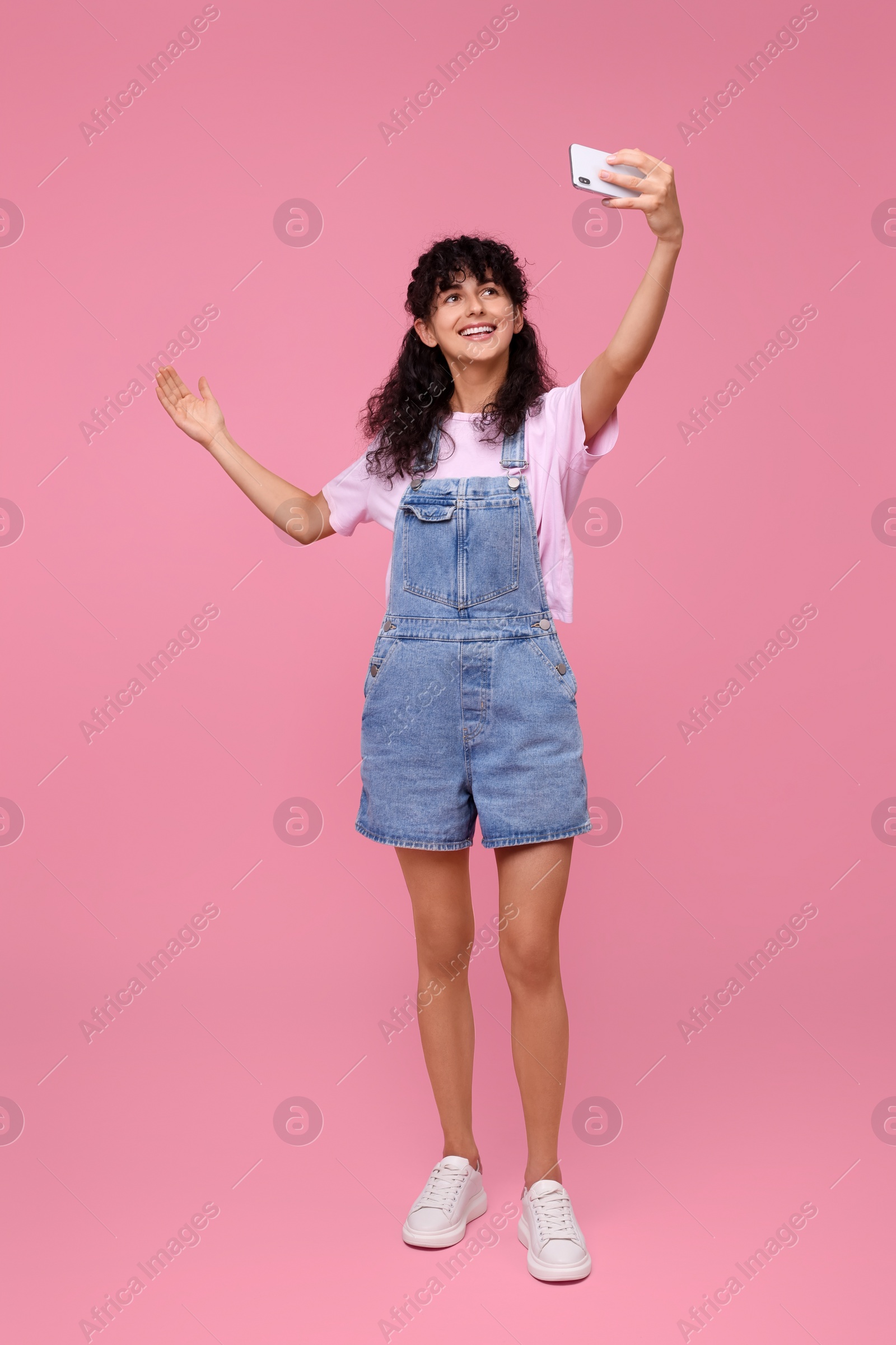 Photo of Beautiful young woman taking selfie on pink background