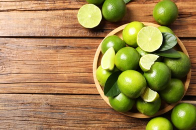 Photo of Fresh limes and green leaves on wooden table, top view. Space for text