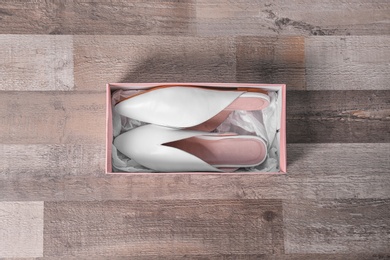 Pair of female shoes in box on wooden background, top view