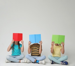 Little children with books sitting on grey background. Reading concept