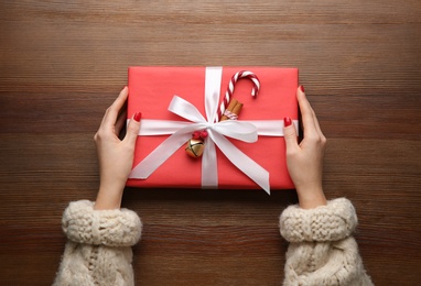 Photo of Woman holding red Christmas gift box at wooden table, top view