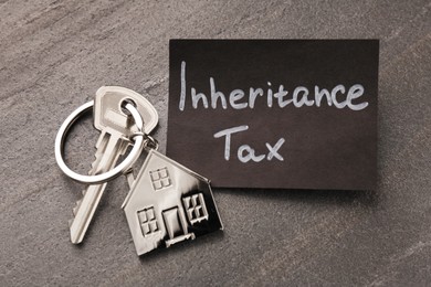 Photo of Inheritance Tax. Card and key with key chain in shape of house on grey table, top view