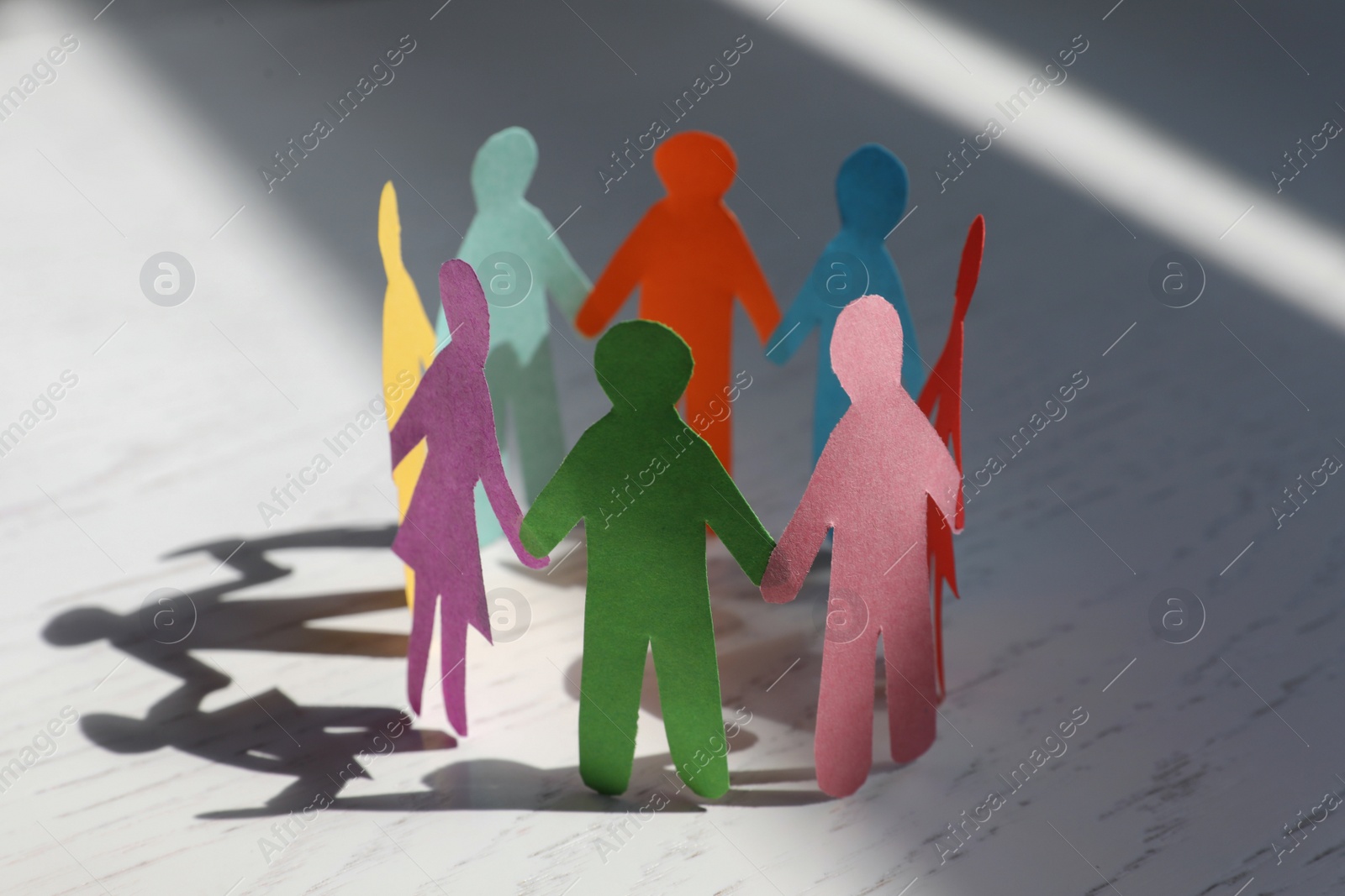 Photo of Paper human figures making circle on white wooden table. Diversity and inclusion concept