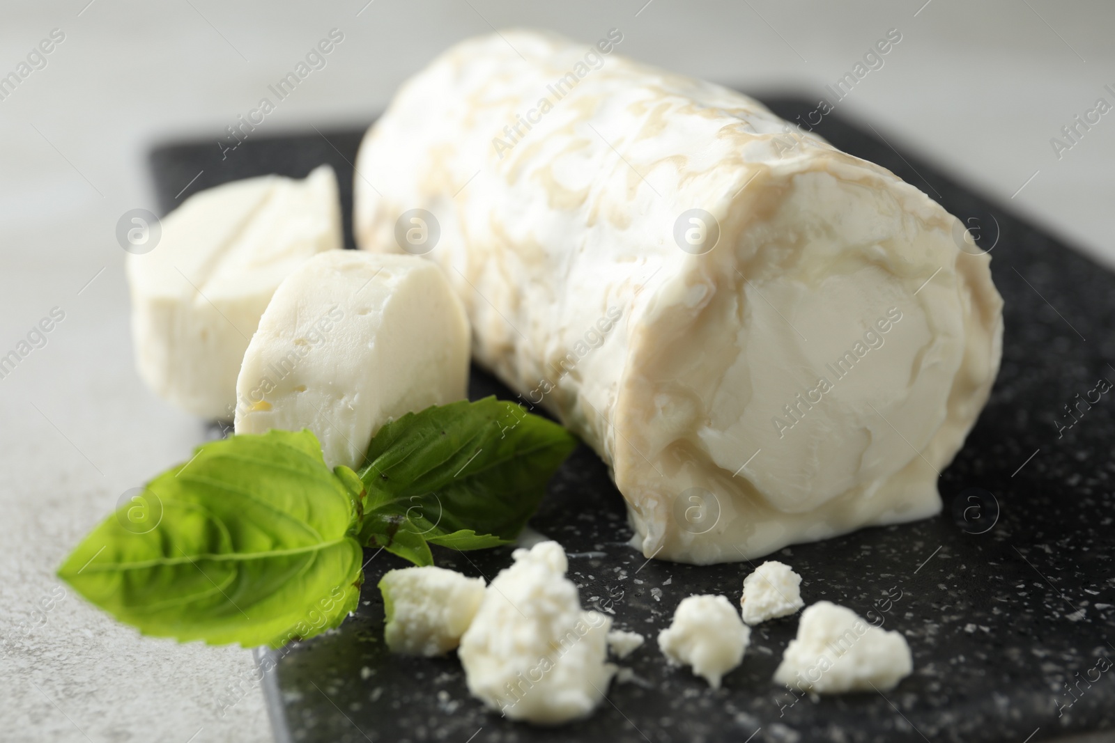 Photo of Delicious fresh goat cheese with basil on black board, closeup