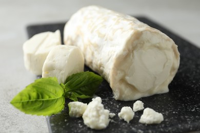 Photo of Delicious fresh goat cheese with basil on black board, closeup