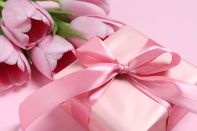 Photo of Beautiful gift box with bow and tulips on pink background, closeup