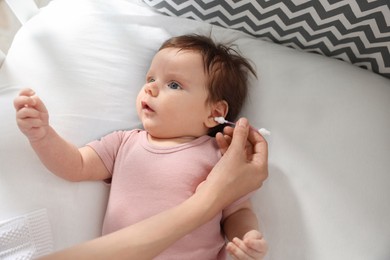 Photo of Mother cleaning ears of her baby with cotton bud on bed, closeup