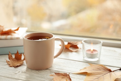 Photo of Cup of tea, autumn leaves and stack of books on windowsill