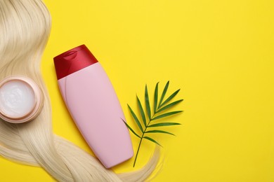 Photo of Lock of healthy blond hair, cosmetic products and green twig on yellow background, flat lay. Space for text