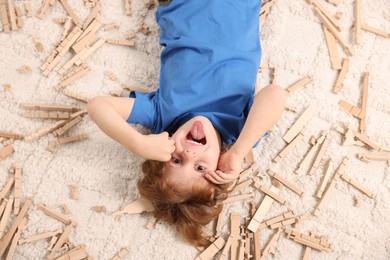 Cute little boy surrounded by wooden construction set on carpet at home, top view. Child`s toy