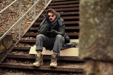 Poor young man sitting on stairs outdoors