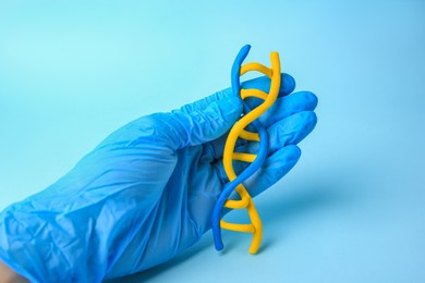 Scientist with DNA molecule model made of colorful plasticine on light blue background, closeup