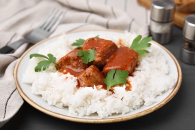 Photo of Delicious goulash served with rice on grey wooden table, closeup