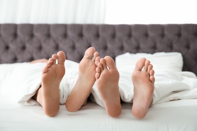 Photo of Gay couple cuddling under blanket on bed, closeup of feet
