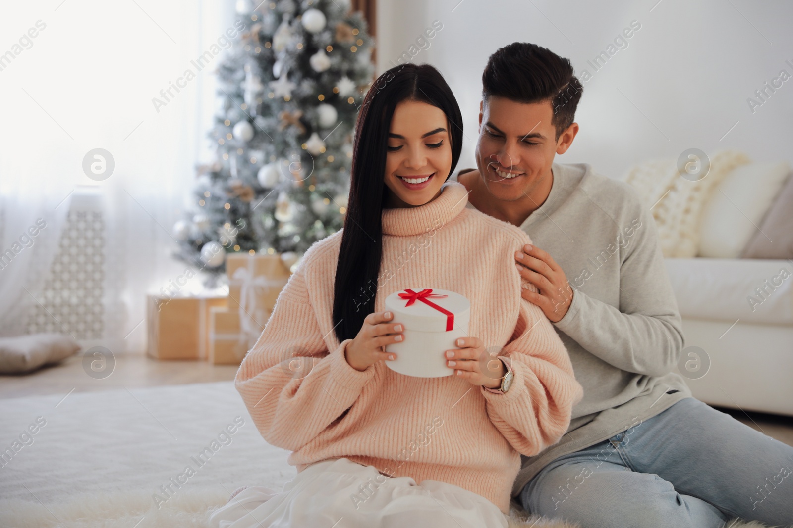 Photo of Couple holding gift box in room with Christmas tree