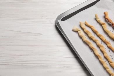 Photo of Baking sheet with homemade breadsticks on white wooden table, top view with space for text. Cooking traditional grissini