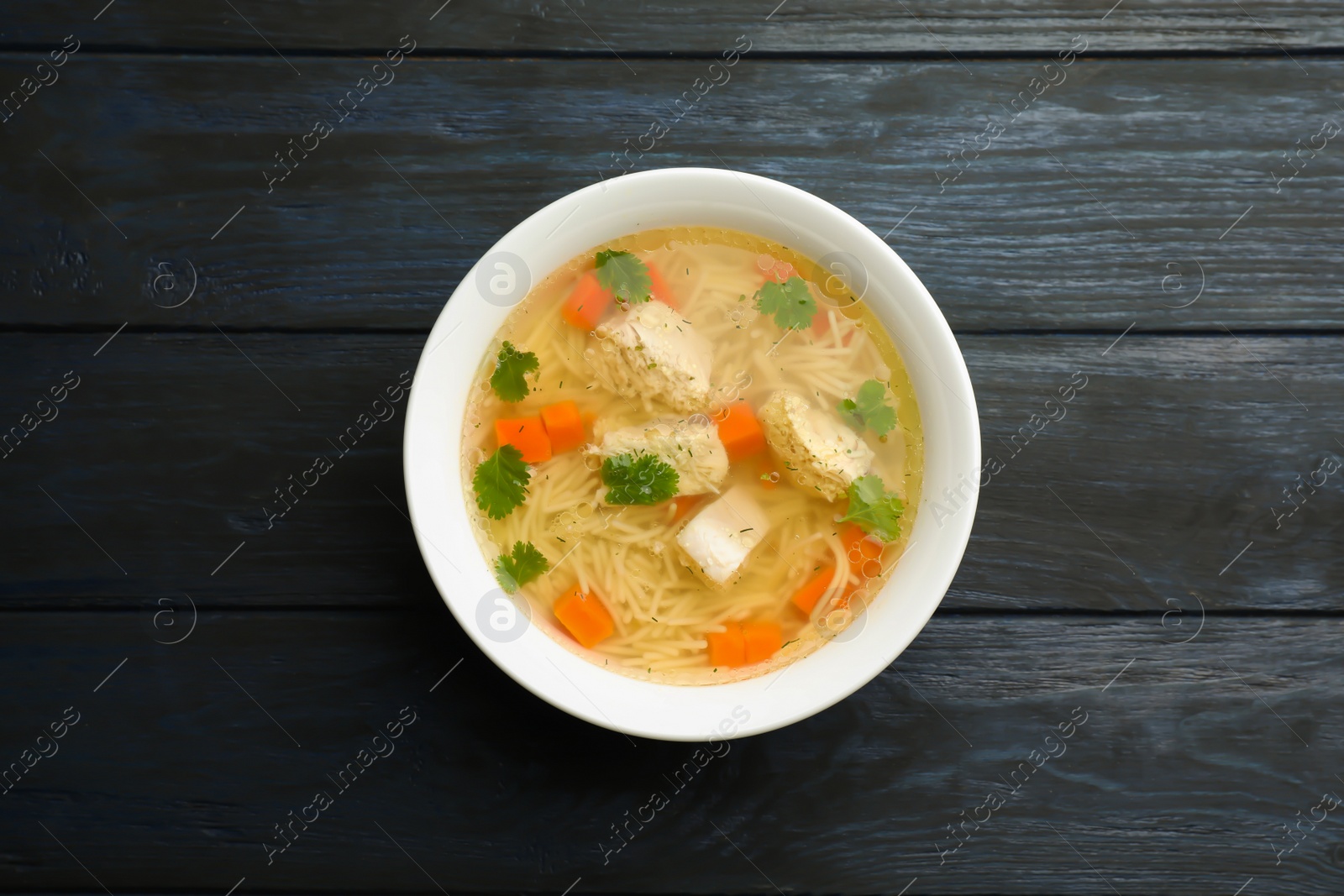 Photo of Dish with fresh homemade chicken soup on wooden  background, top view