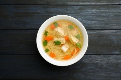 Photo of Dish with fresh homemade chicken soup on wooden  background, top view