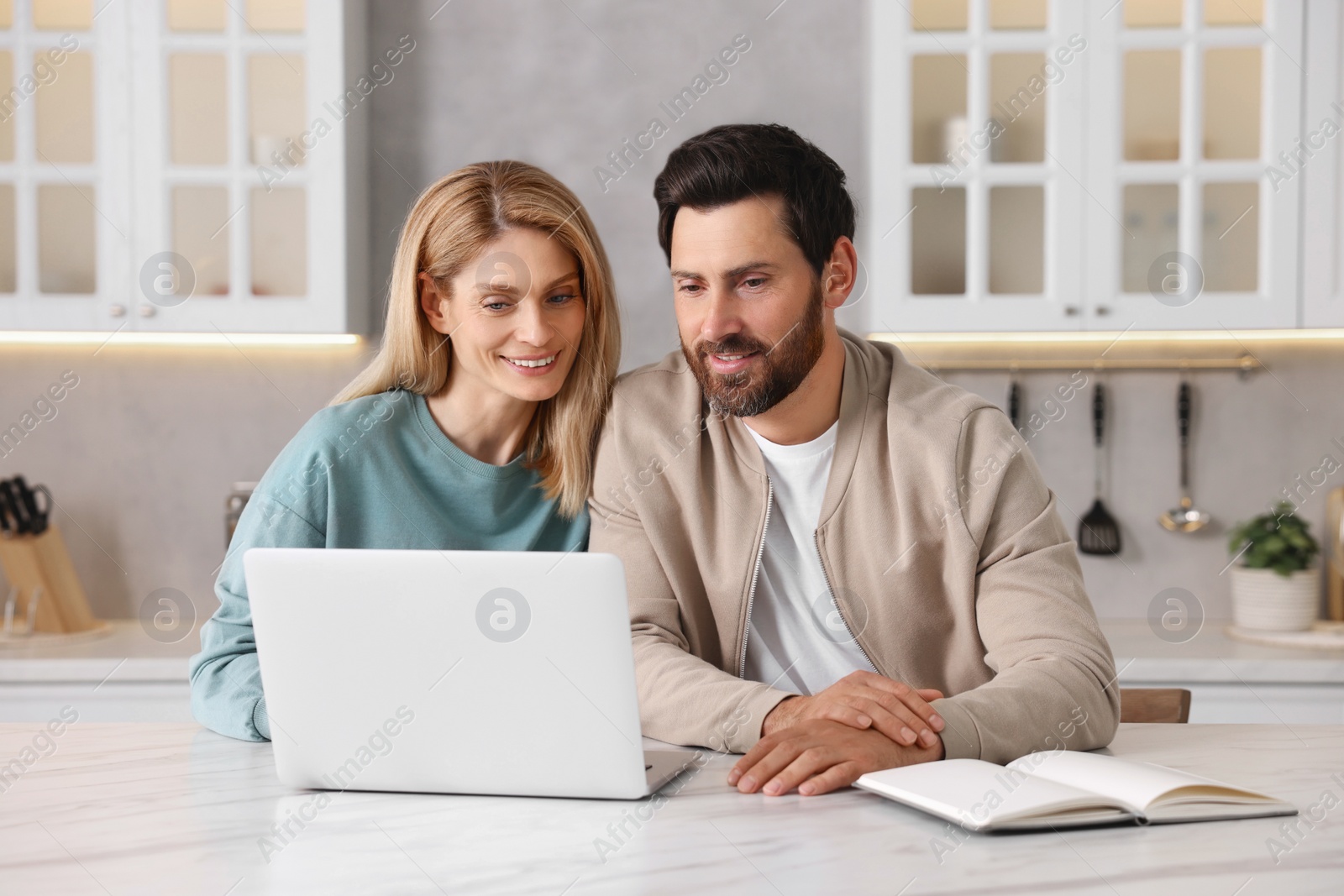 Photo of Happy couple with laptop at white table in kitchen