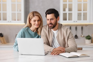 Photo of Happy couple with laptop at white table in kitchen