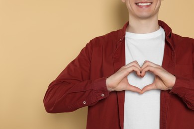 Photo of Happy volunteer making heart with his hands on beige background, closeup