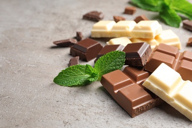 Photo of Different kinds of chocolate with mint on gray table