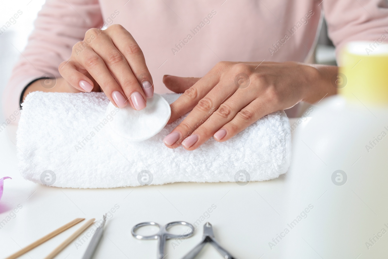 Photo of Woman removing polish from nails with cotton pad at table, closeup