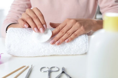 Woman removing polish from nails with cotton pad at table, closeup