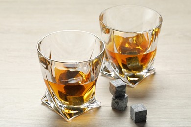 Whiskey stones and drink in glasses on light wooden table, closeup