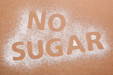 Photo of Phrase No Sugar made of granules on brown background, flat lay