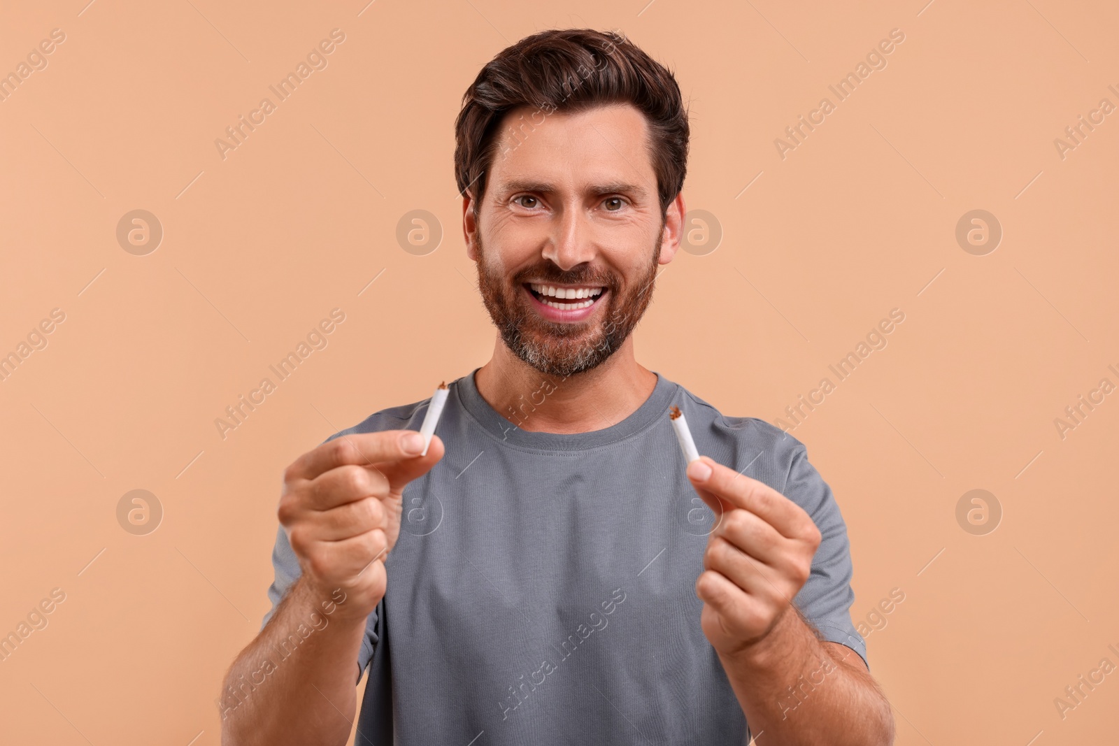 Photo of Stop smoking concept. Happy man holding pieces of broken cigarette on light brown background