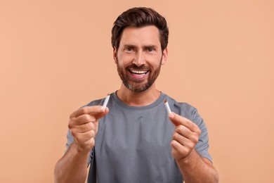 Stop smoking concept. Happy man holding pieces of broken cigarette on light brown background