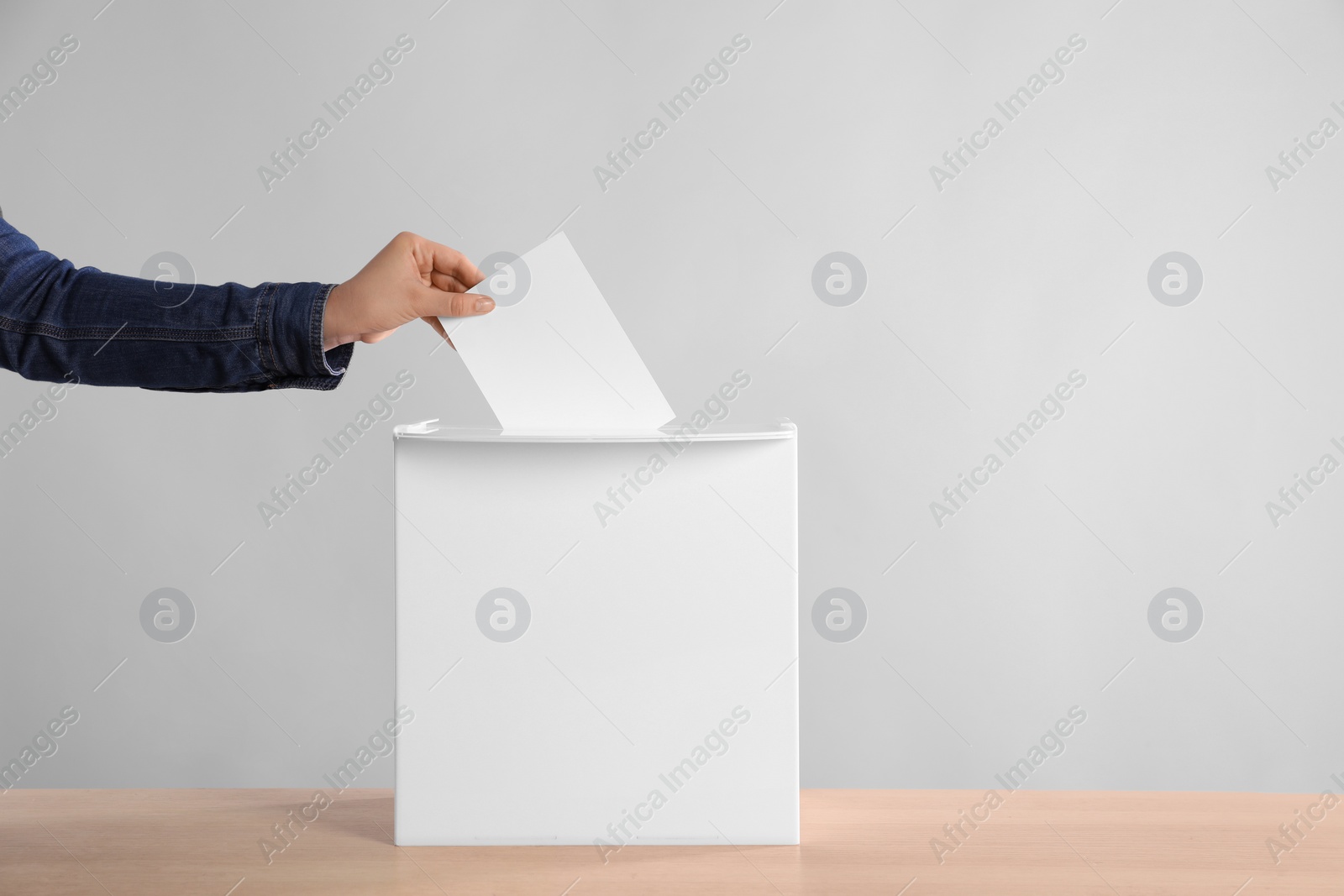 Photo of Woman putting her vote into ballot box on wooden table against light grey background, closeup. Space for text