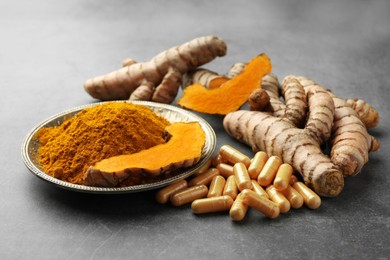 Photo of Aromatic turmeric powder, pills and raw roots on grey table