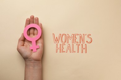 Photo of Girl holding female gender sign near text Women's Health on beige background, top view