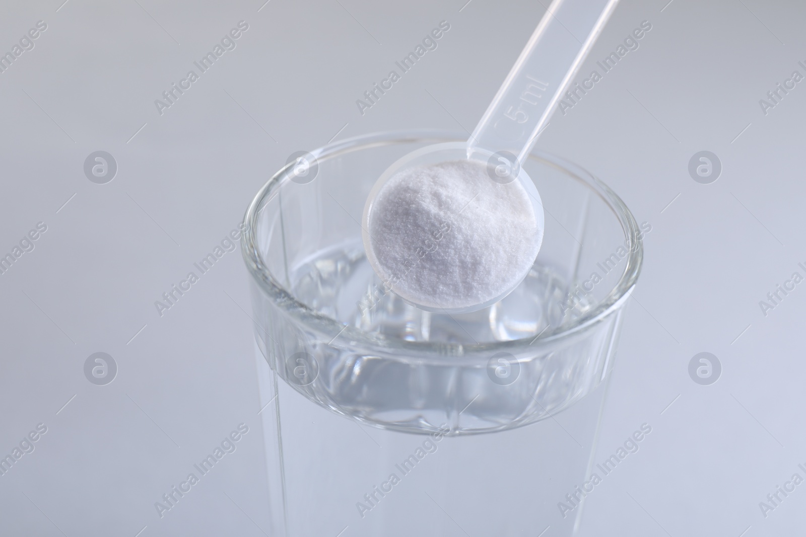 Photo of Adding baking soda into glass of water on light grey background, closeup