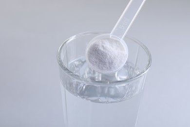 Adding baking soda into glass of water on light grey background, closeup